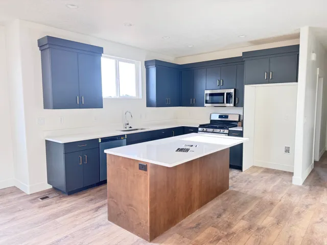 Kitchen with stainless steel appliances, a kitchen island, light wood-type flooring, blue cabinets, and recessed lighting