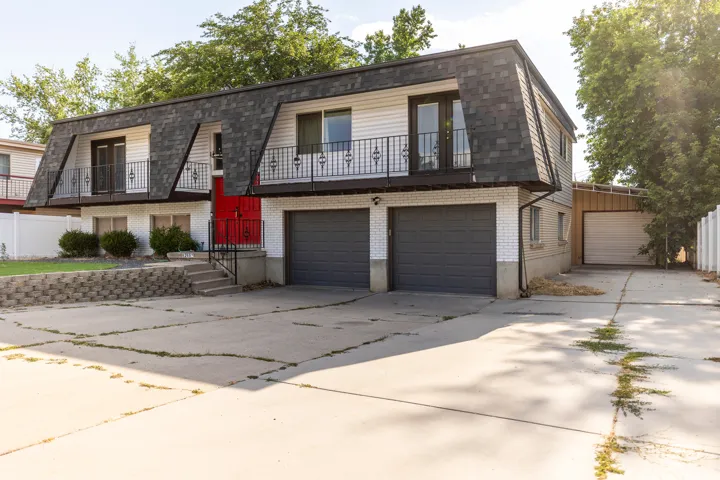 View of front of home with a balcony, mansard roof, brick siding, and concrete driveway