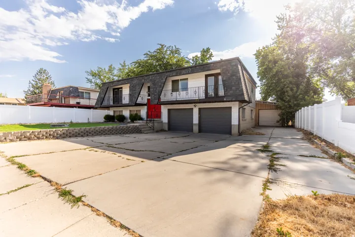 View of front of home with mansard roof, brick siding, concrete driveway, a balcony, and roof with shingles