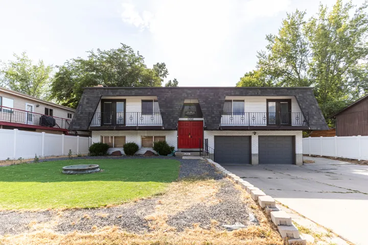 View of property featuring a balcony, brick siding, concrete driveway, mansard roof, and an attached garage