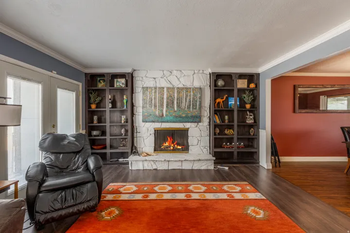 Living room with ornamental molding, dark wood finished floors, a fireplace, a textured ceiling, and built in shelves