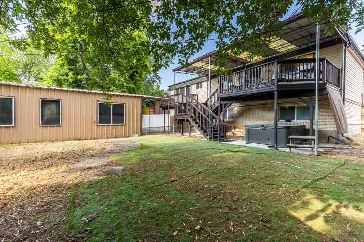 Back of property with a hot tub, a patio area, stairs, a deck, and brick siding