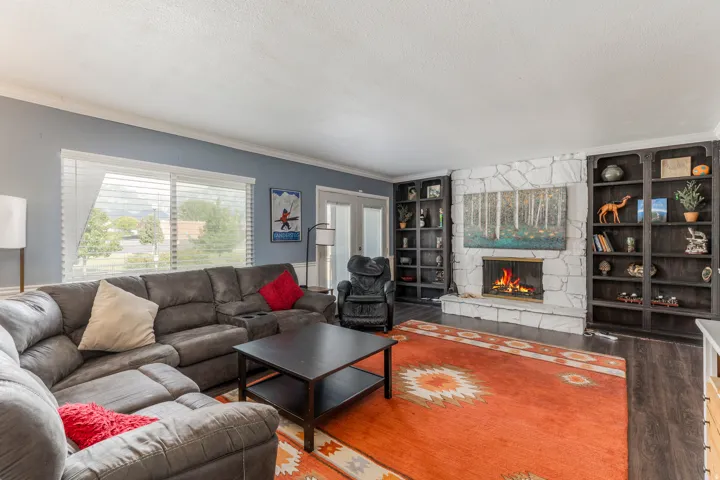 Living room with built in shelves, wood finished floors, crown molding, a stone fireplace, and a textured ceiling