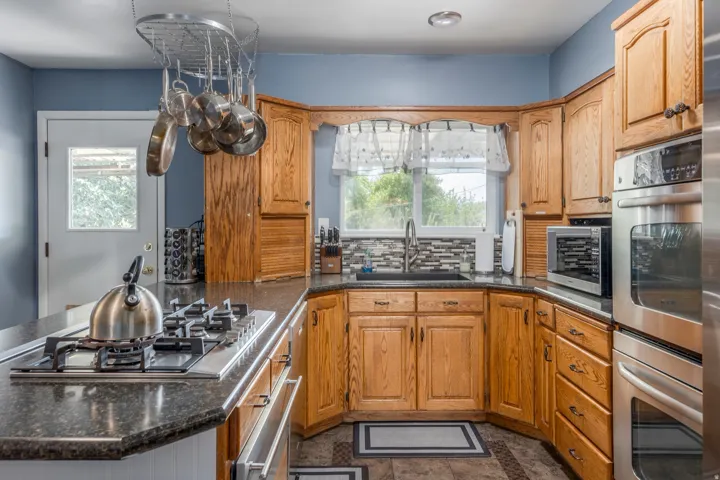Kitchen featuring stainless steel appliances, tasteful backsplash, dark stone countertops, and plenty of natural light