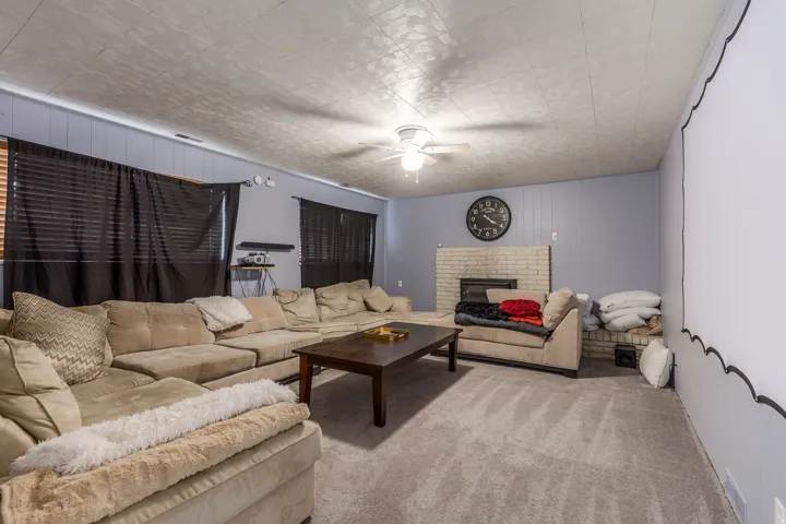 Carpeted living room featuring a brick fireplace, wooden walls, and a ceiling fan
