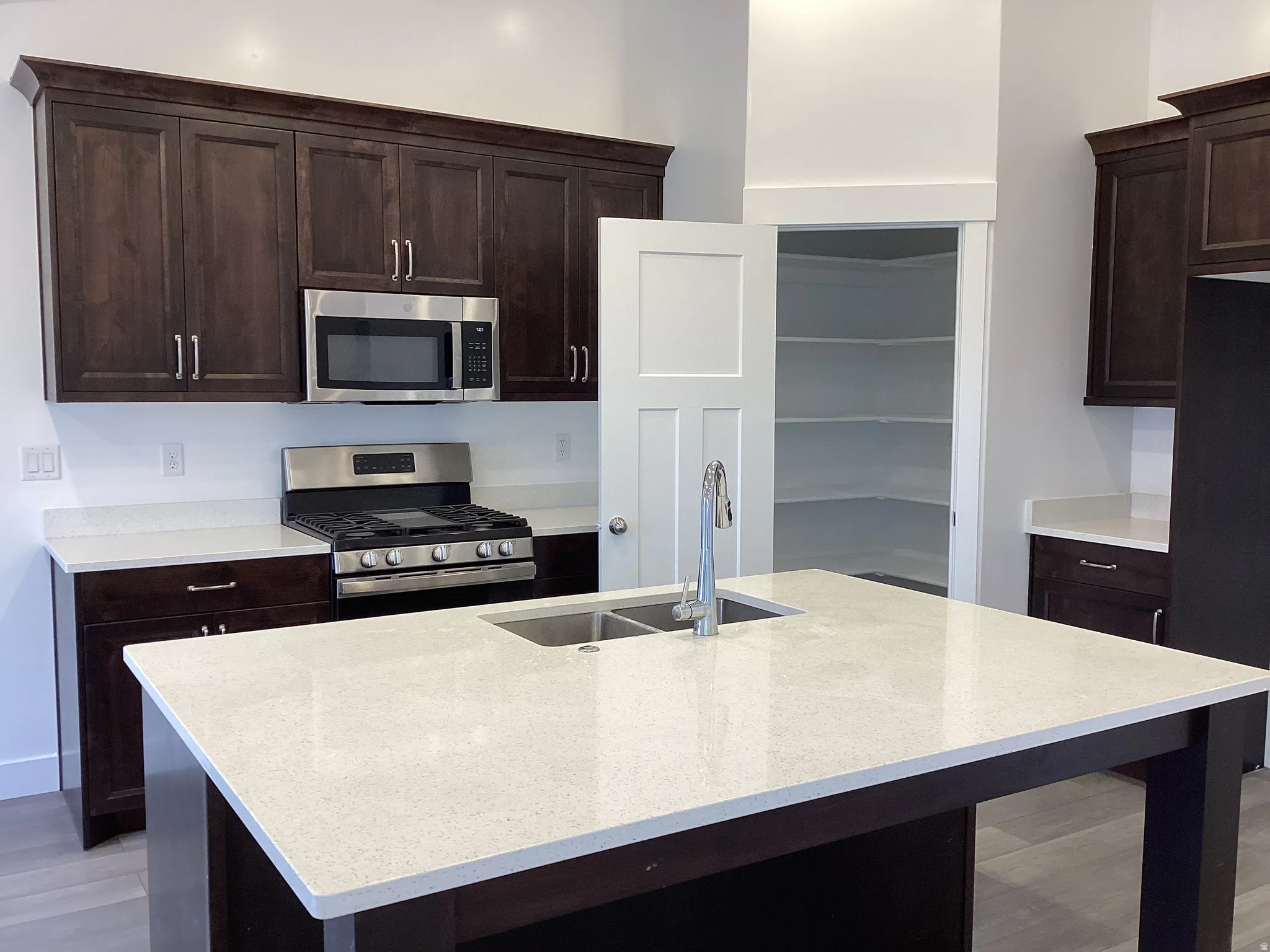 Kitchen with stainless steel appliances, dark wood finish cabinetry, light stone countertops, and light wood-type flooring
