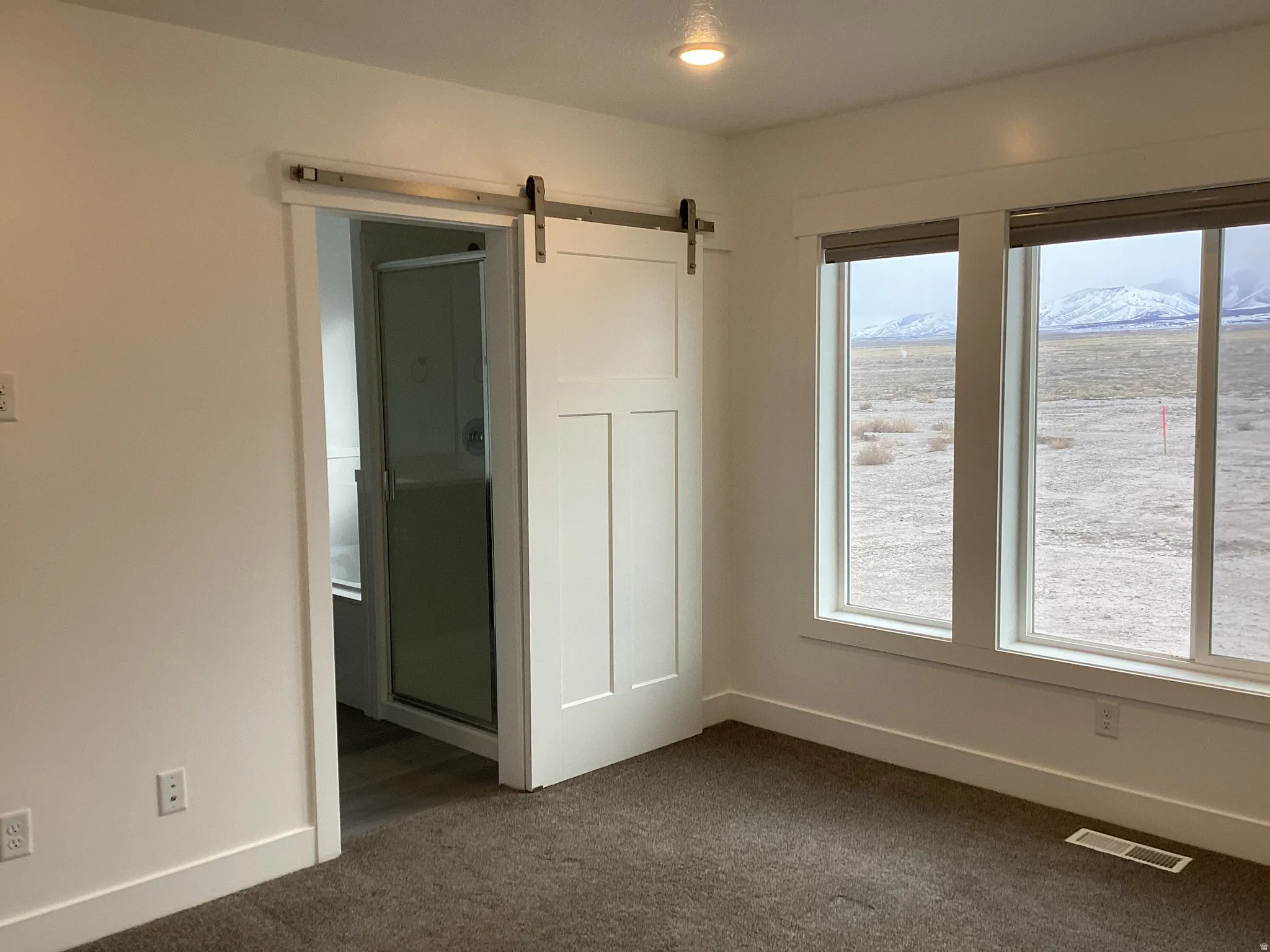 Unfurnished bedroom with a barn door, dark carpet, and a mountain view