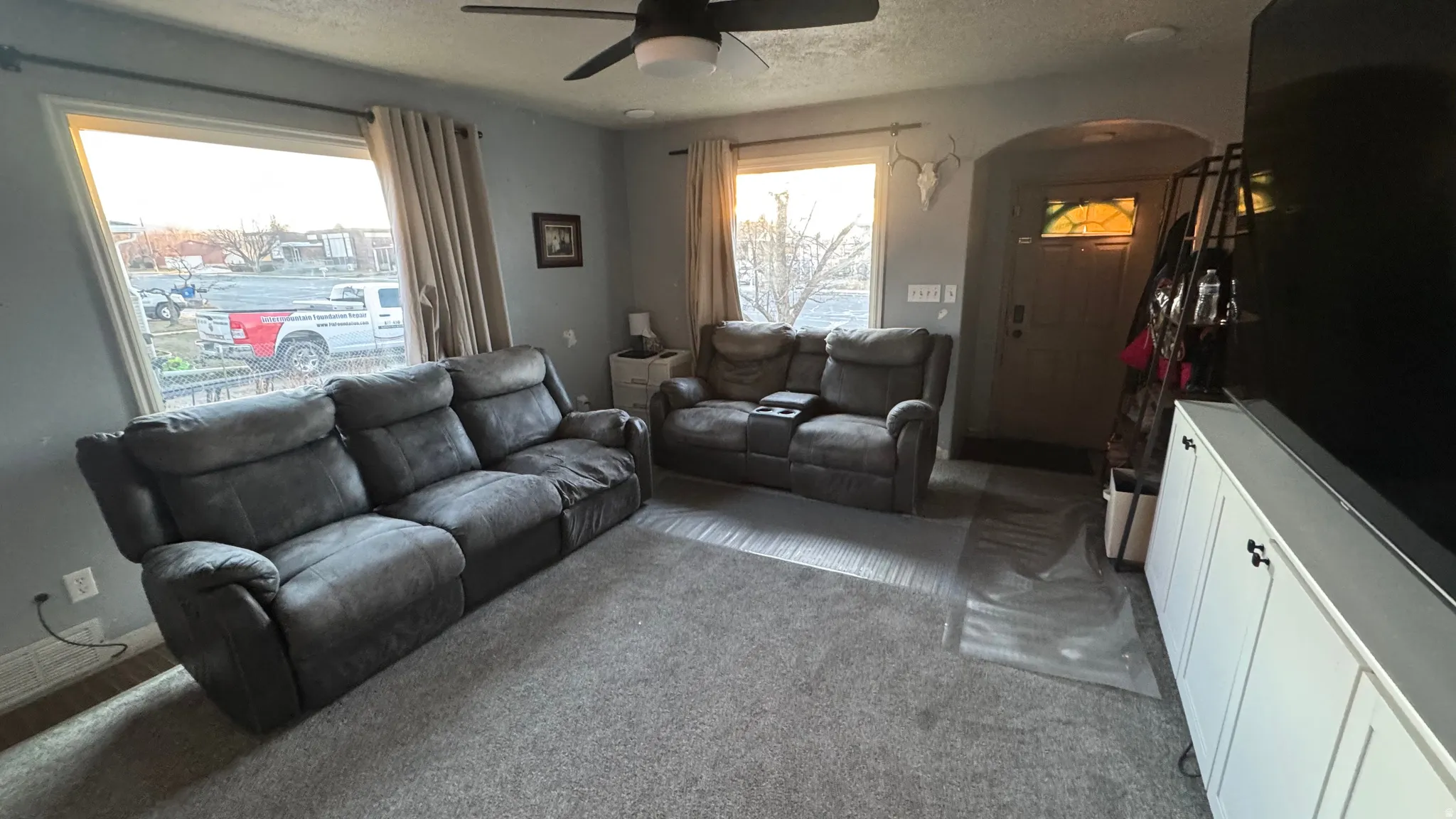 Living room featuring a ceiling fan, arched walkways, carpet, and a textured ceiling