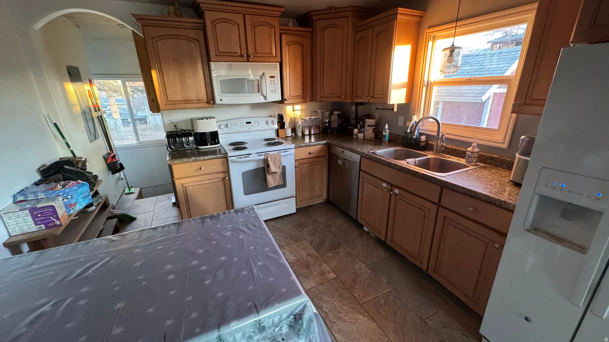 Kitchen with white appliances, brown cabinets, arched walkways, and dark stone counters