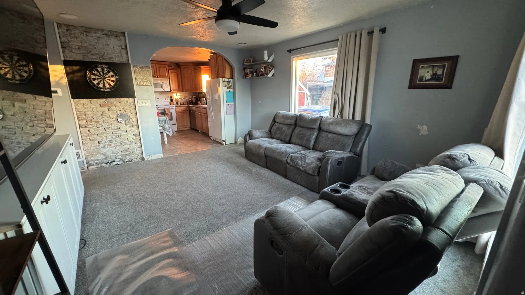 Living room featuring light colored carpet, arched walkways, a ceiling fan, and a textured ceiling