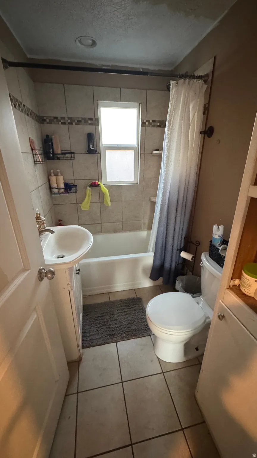 Bathroom with vanity, shower / bath combination with curtain, light tile patterned floors, and a textured ceiling