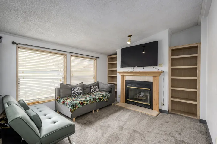 Carpeted living area with vaulted ceiling, a textured ceiling, a tile fireplace, and built in shelves