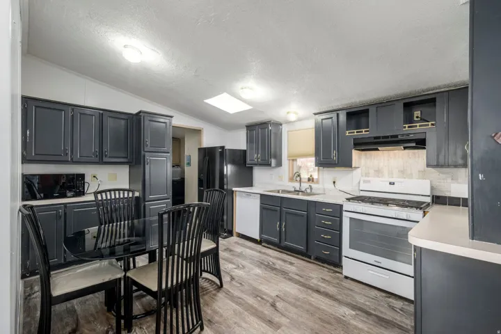 Kitchen featuring white appliances, light countertops, a textured ceiling, under cabinet range hood, and vaulted ceiling