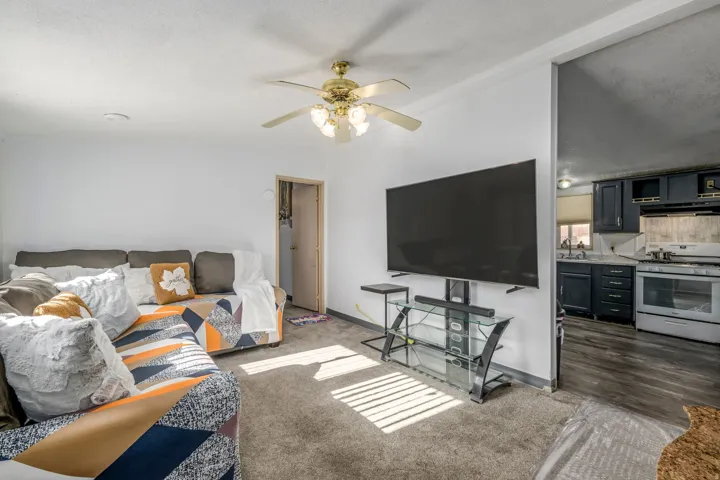 Living room featuring ceiling fan, a textured ceiling, and dark carpet