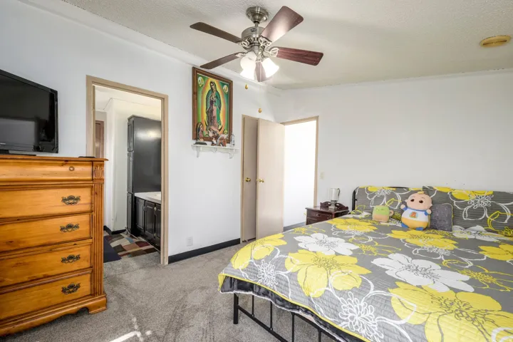 Bedroom with light colored carpet, a textured ceiling, a ceiling fan, ensuite bath, and freestanding refrigerator