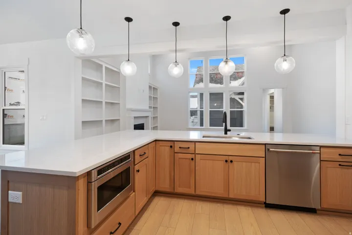 Kitchen featuring stainless steel appliances, light wood-type flooring, decorative light fixtures, and light stone countertops