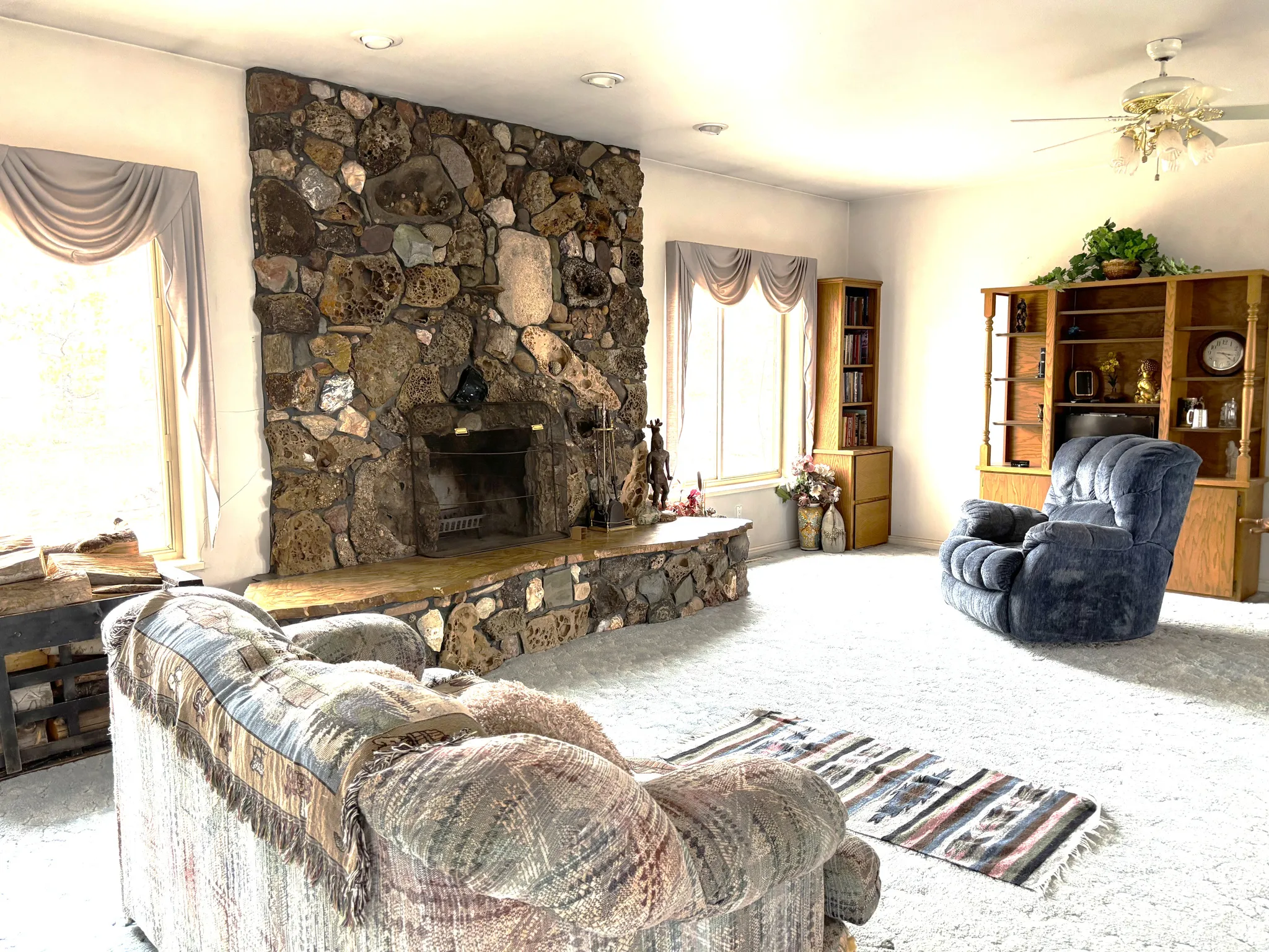 Living area featuring a stone fireplace, ceiling fan, and carpet floors