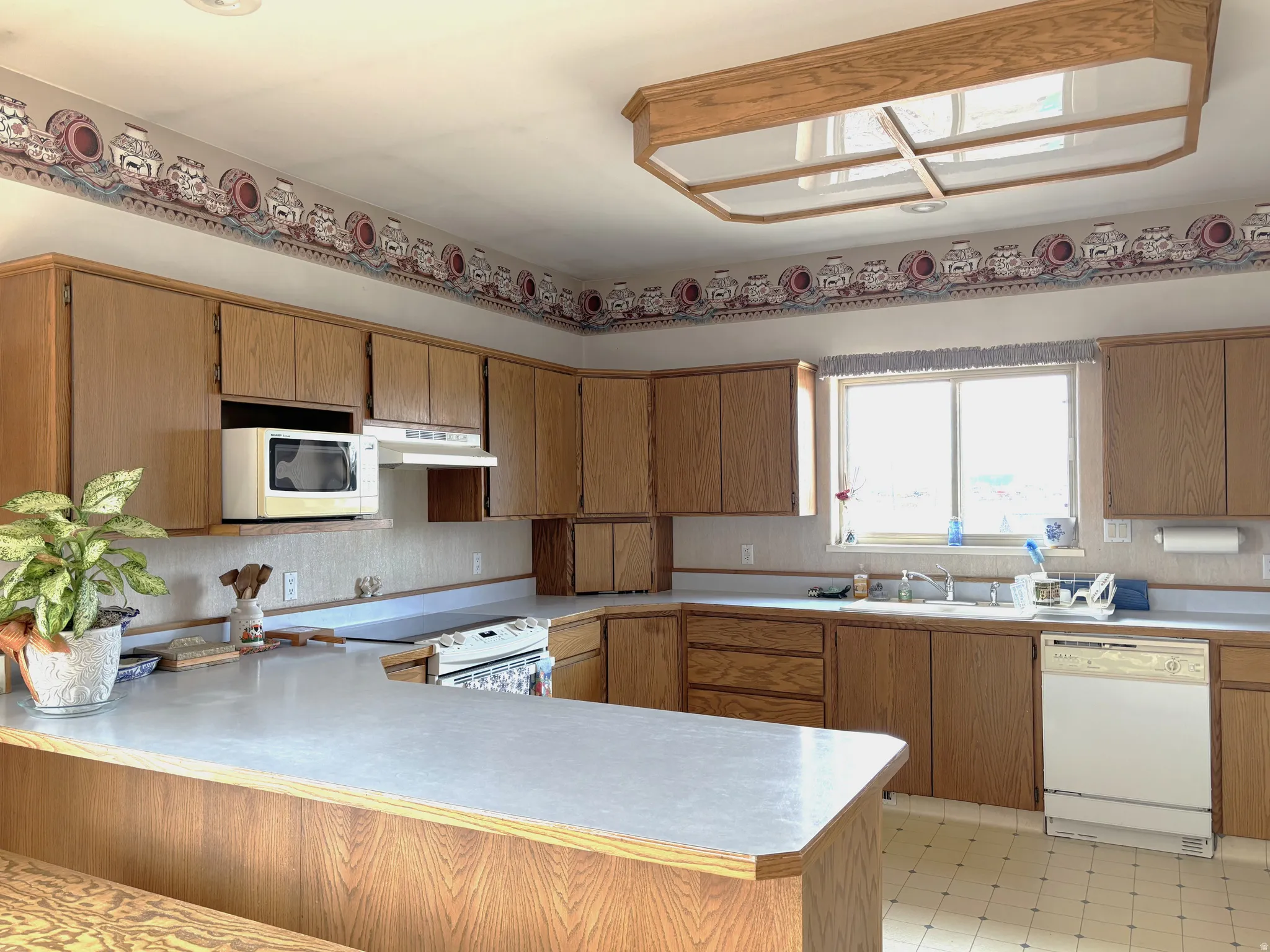 Kitchen with brown cabinetry, light floors, light countertops, white appliances, and a peninsula