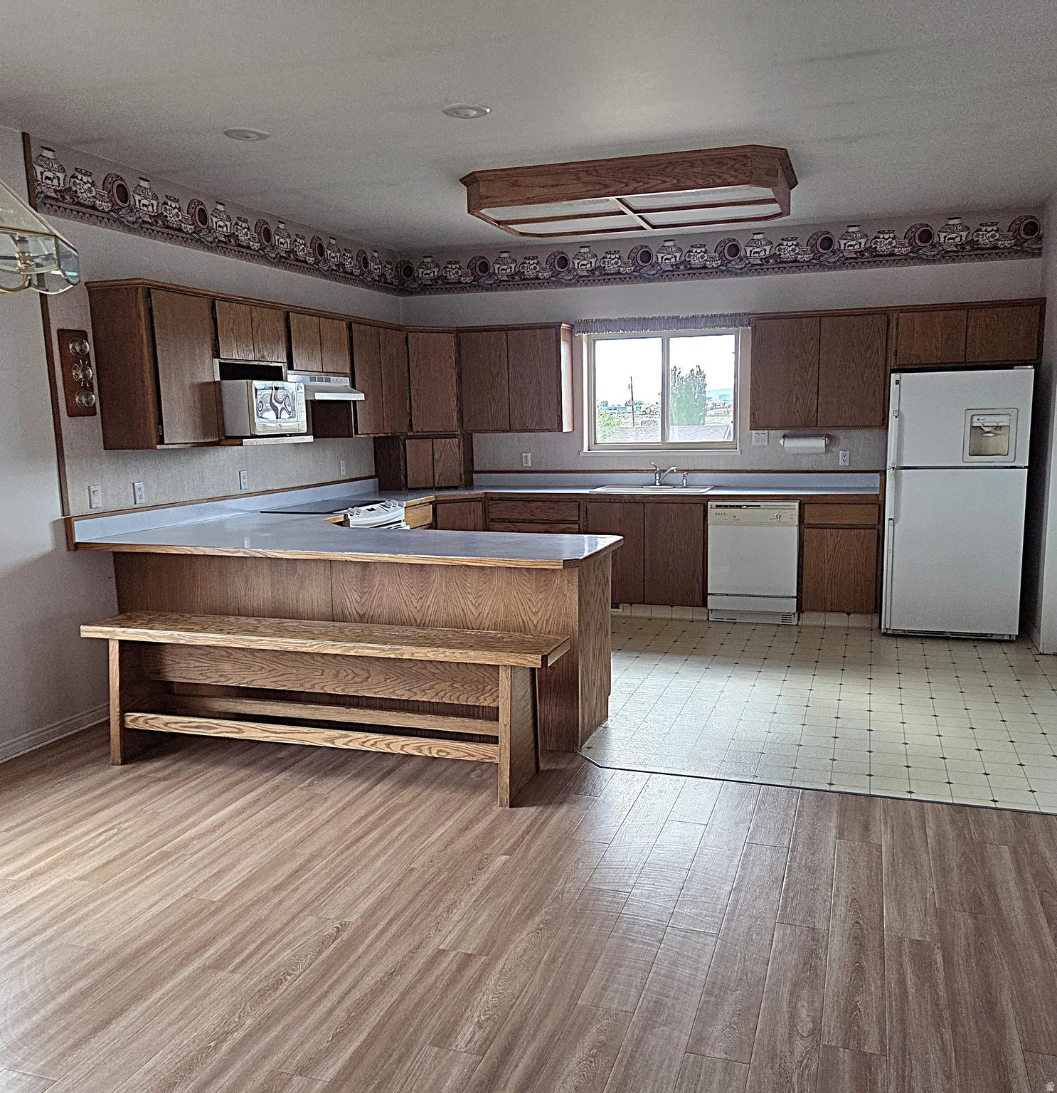 Kitchen featuring a peninsula, white appliances, light countertops, and light wood-style floors