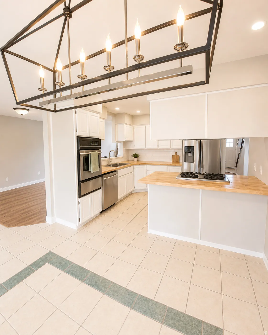Kitchen featuring white cabinetry, wood-finish countertops, stainless steel appliances, and tile flooring with a decorative border