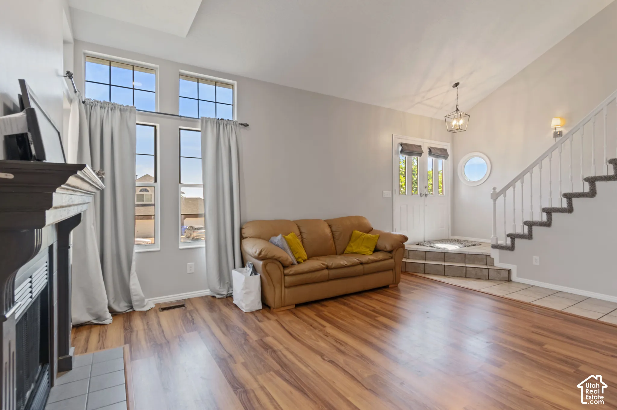 Living area featuring vaulted ceiling, stairway, light wood finished floors, a fireplace with flush hearth, and a chandelier