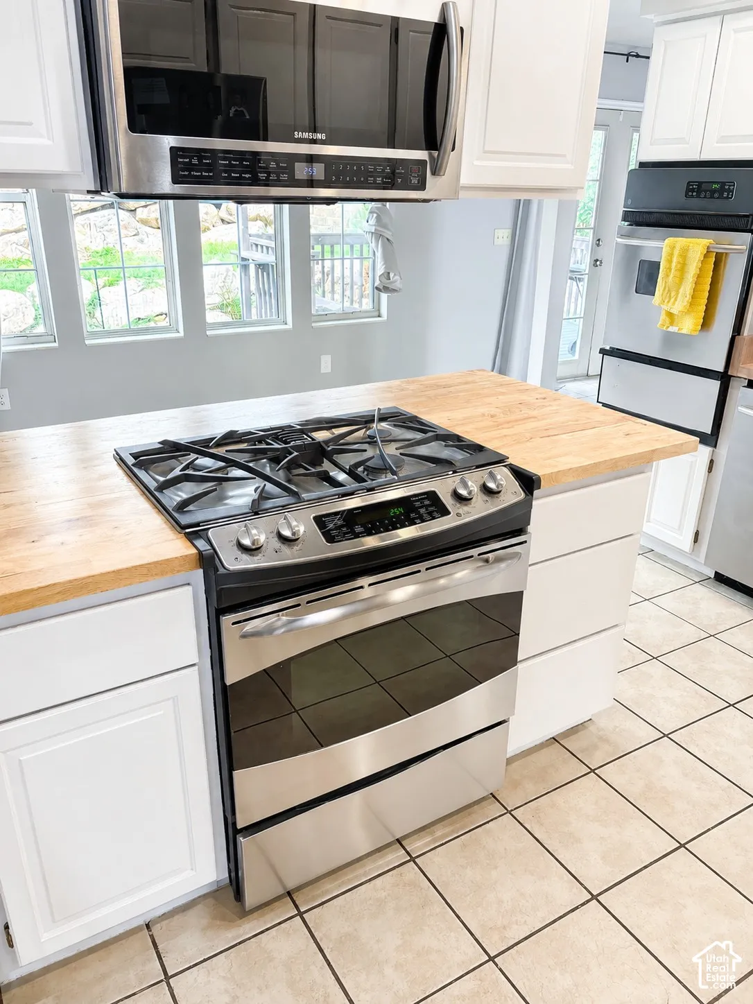 Stainless steel range with gas cooktop, wood-finish countertop island, white cabinetry, stainless steel microwave, and tile flooring