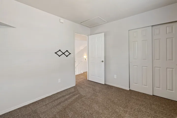 Unfurnished bedroom with dark colored carpet, attic access, and a closet