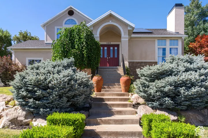 View of front of home featuring solar panels, stucco siding, a chimney, and roof with shingles