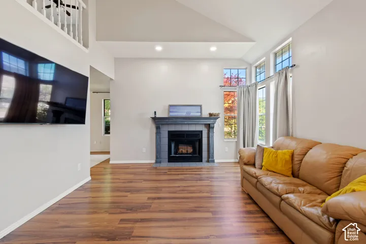 Living area with a tile fireplace, wood finished floors, high vaulted ceiling, recessed lighting, and healthy amount of natural light