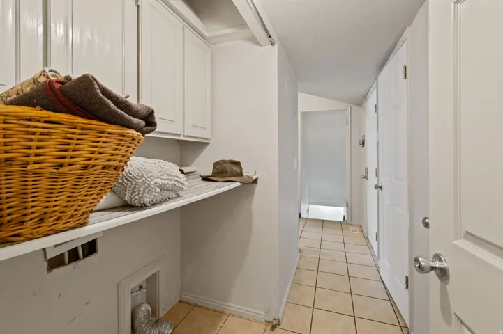 Laundry area with cabinet space, light tile patterned flooring, and lofted ceiling