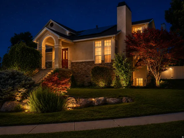 Stucco and stone exterior featuring a covered entry porch, a red front door, multiple windows, and a landscaped front yard with decorative boulders