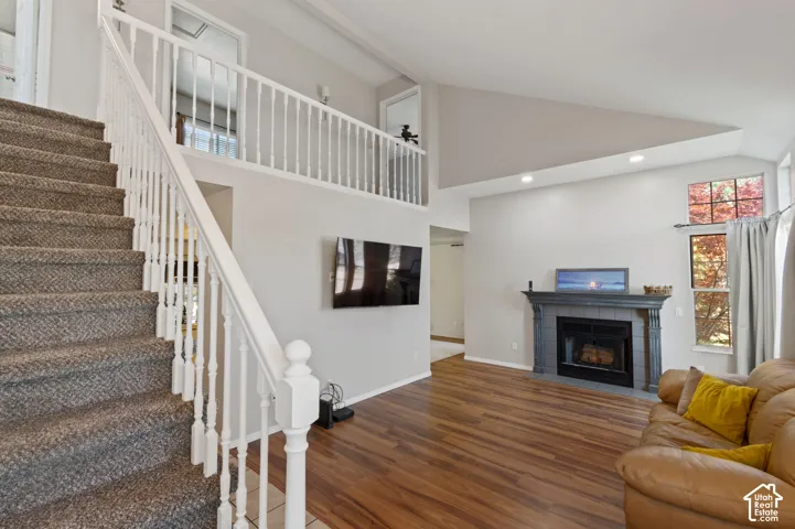 Living room with wood finished floors, a tile fireplace, recessed lighting, and high vaulted ceiling