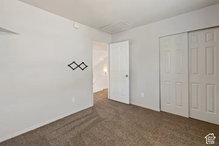 Unfurnished bedroom with dark colored carpet, attic access, and a closet