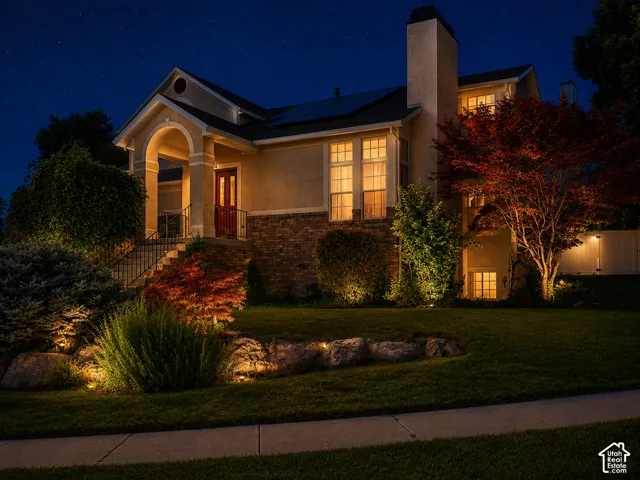 Stucco and stone exterior featuring a covered entry porch, a red front door, multiple windows, and a landscaped front yard with decorative boulders