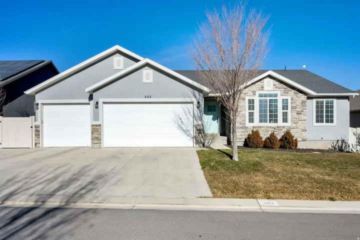 Single story home with stone siding, a garage, driveway, a front yard, and stucco siding