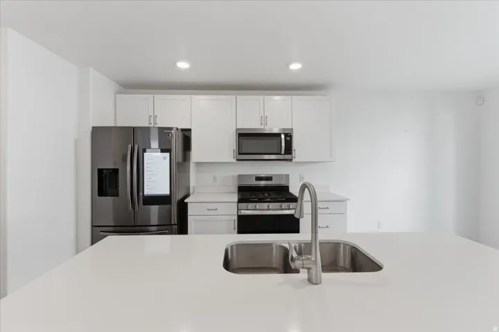 Kitchen featuring appliances with stainless steel finishes, white cabinetry, recessed lighting, and light stone counters