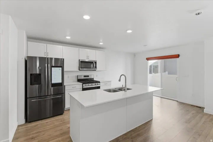 Kitchen featuring appliances with stainless steel finishes, white cabinets, light wood-style floors, a center island with sink, and recessed lighting