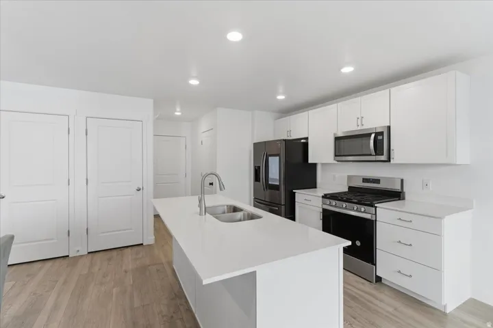 Kitchen with appliances with stainless steel finishes, white cabinets, a kitchen island with sink, light wood-type flooring, and recessed lighting