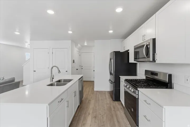 Kitchen with stainless steel appliances, a center island with sink, white cabinets, light wood-style floors, and light stone countertops