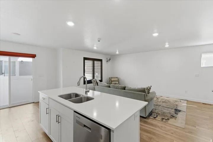 Kitchen featuring white cabinetry, dishwasher, light wood finished floors, a kitchen island with sink, and open floor plan