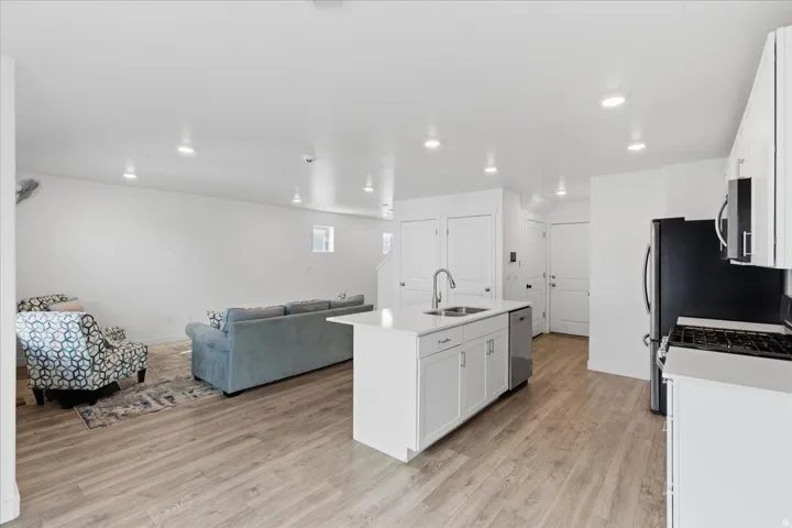 Kitchen with white cabinets, open floor plan, a kitchen island with sink, light wood-style flooring, and recessed lighting