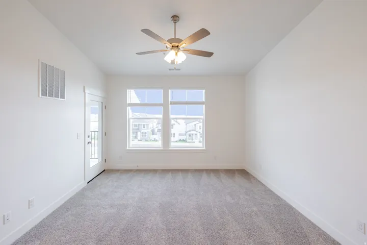 Spacious room featuring neutral carpeting, a ceiling fan with integrated lighting, and multiple windows providing natural light
