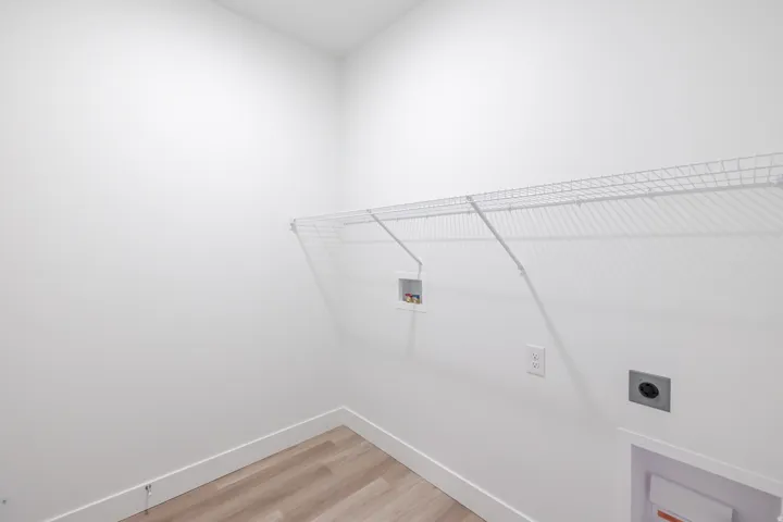 Utility area featuring light wood-finish flooring, white baseboards, and a white wire shelving unit