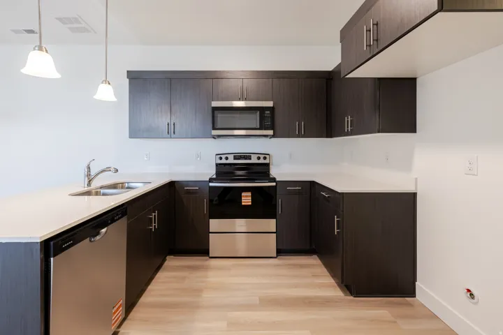 Modern kitchen featuring dark wood-finish cabinetry, light-toned countertops, and stainless steel appliances including a range, microwave, and dishwasher