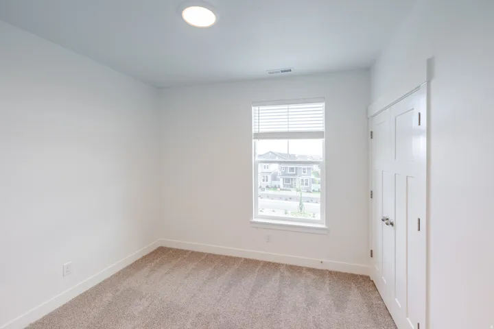 Neutral tone walls and carpeting throughout, featuring a single window with blinds and a flush-mount ceiling light fixture