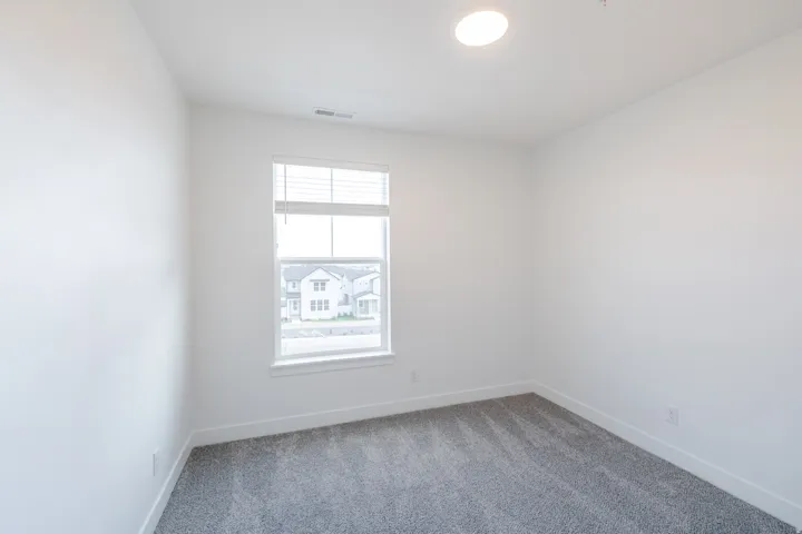 Bright interior space featuring a window with white blinds, neutral gray carpeting, white walls, and a flush-mount ceiling light