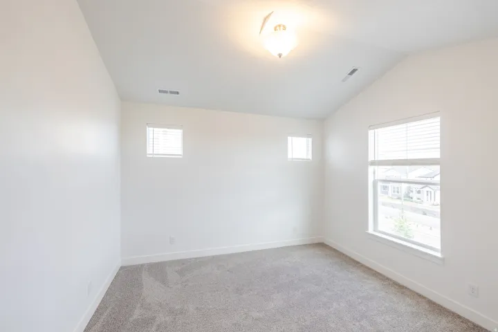 Vaulted ceiling bedroom featuring plush gray carpeting, white walls, and a large window with blinds