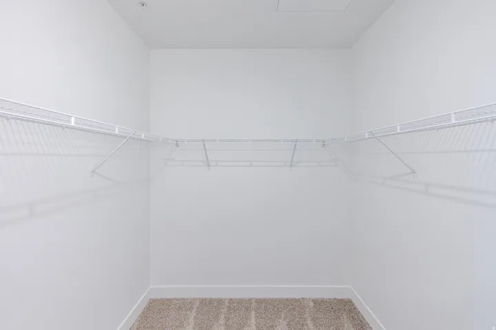 Walk-in closet featuring white wire shelving, neutral carpeting, and white baseboards