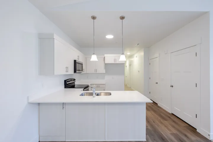 Modern kitchen featuring an integrated island with stainless steel sink, white cabinetry, integrated black appliances, and pendant lighting
