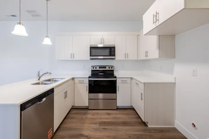 Contemporary kitchen featuring white cabinetry, light-toned countertops, stainless steel appliances, and wood-finish flooring